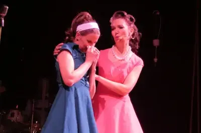 Zwei Schauspielerinnen auf der Bühne, eine tröstet die andere in einem emotionalen Moment.